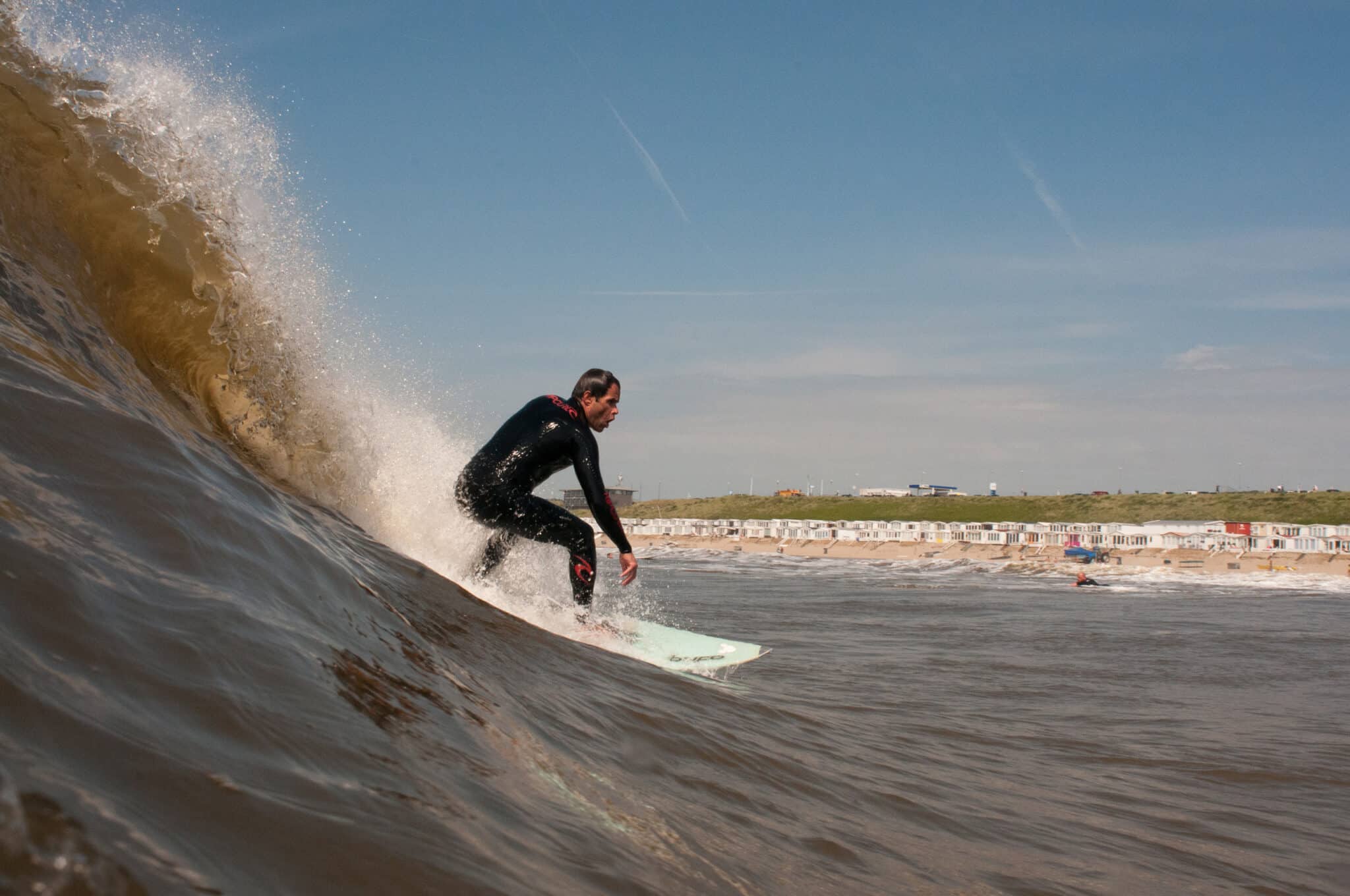 Surfer op zijn board die een golf pakt in de Noordzee voor Zandvoort met het strand op de achtergrond