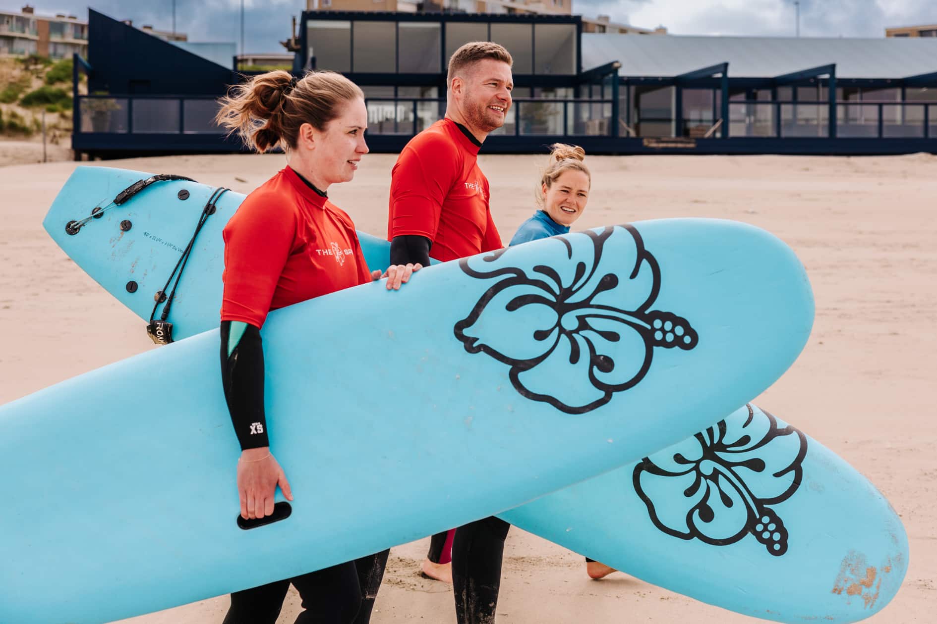 Twee mensen lopen met de instructeur over het strand naar de zee voor een golfsurfles