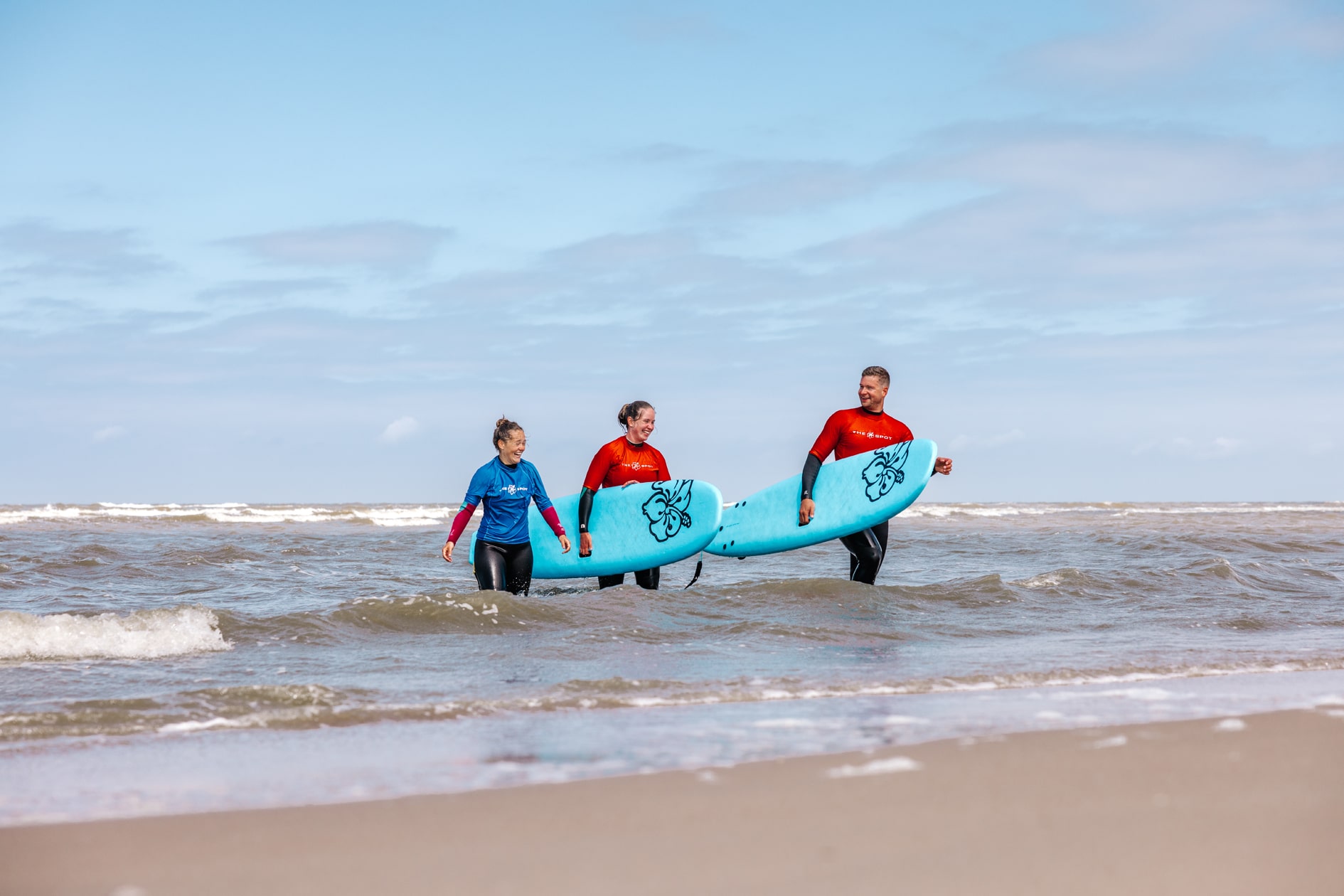 Een man en vrouw lopen na de surfles met hun surfplank uit de zee al pratend met hun surf instructrice
