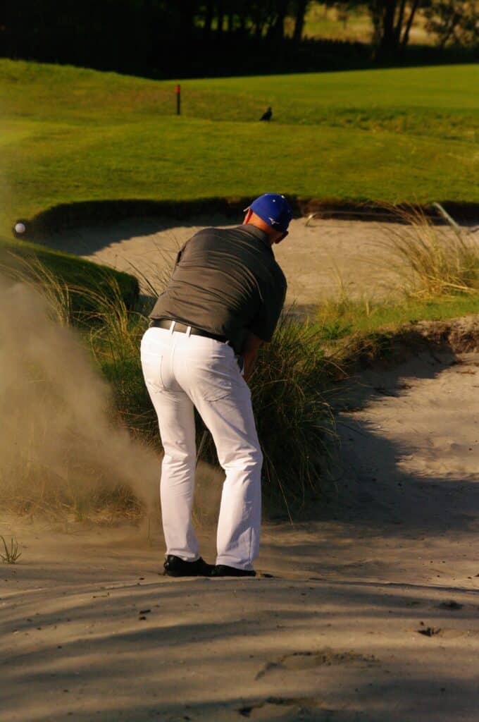 Golfer slaat een balletje uit de bunker, richting de baan.