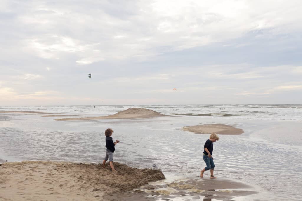 Twee jongetje spelen in hun korte broek op het strand bij de zee op een bewolkte dag in september