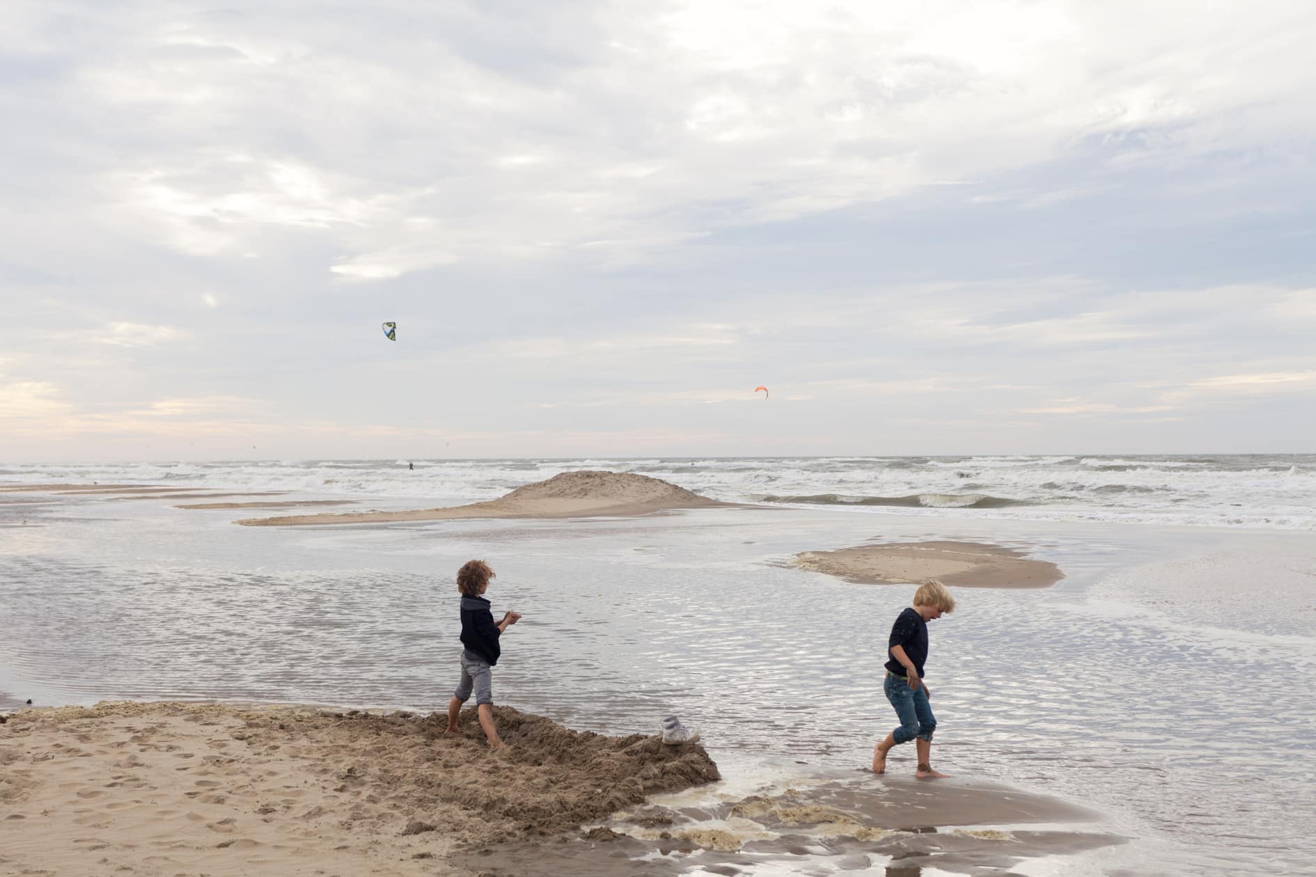 Twee jongetje spelen in hun korte broek op het strand bij de zee op een bewolkte dag in september