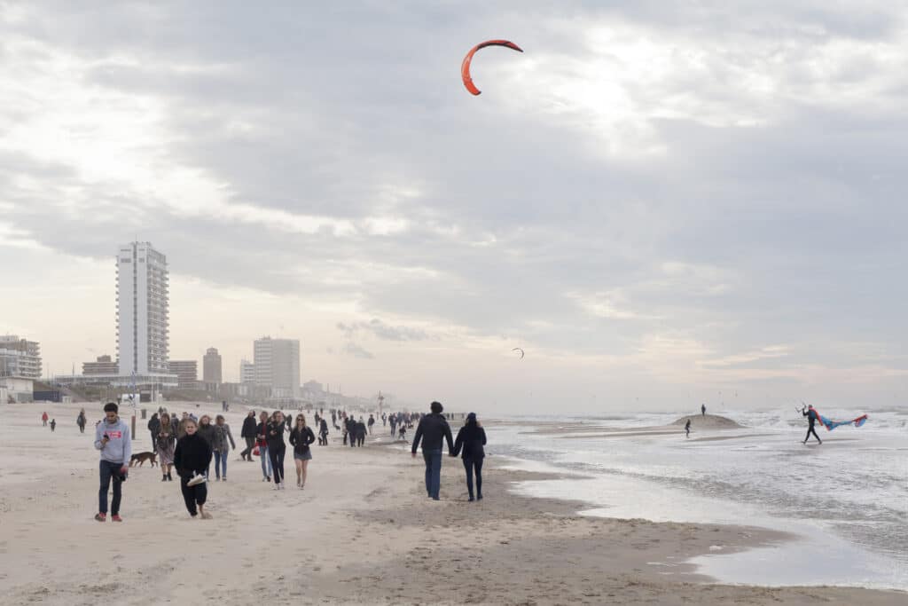 Wandelaars op het strand met een kiter in zee