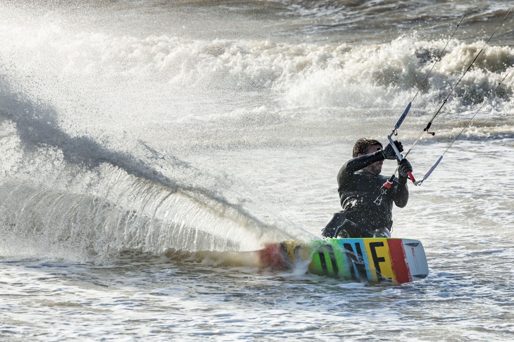 Kitesurfer maak een bocht in het water waarbij het water opspat