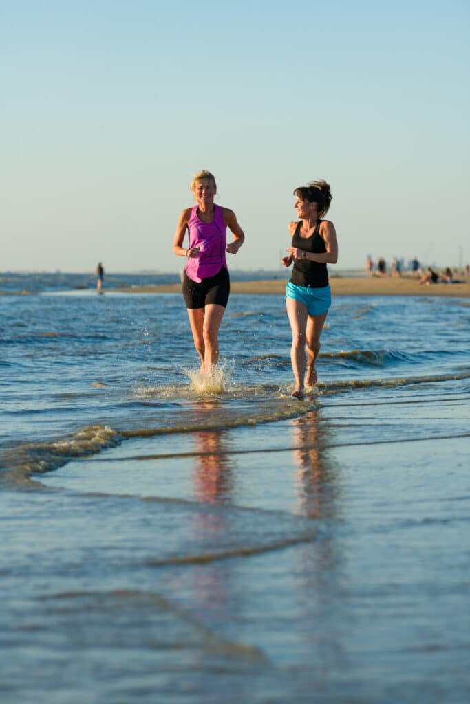 Twee vrouwen zijn aan het hardlopen in de zee op het strand.
