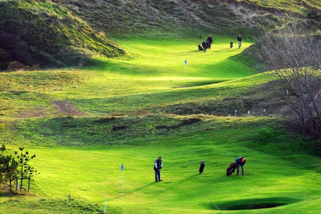 Meerdere golfers lopen een ronde over de groene golfbaan in Zandvoort, gezien van bovenaf.