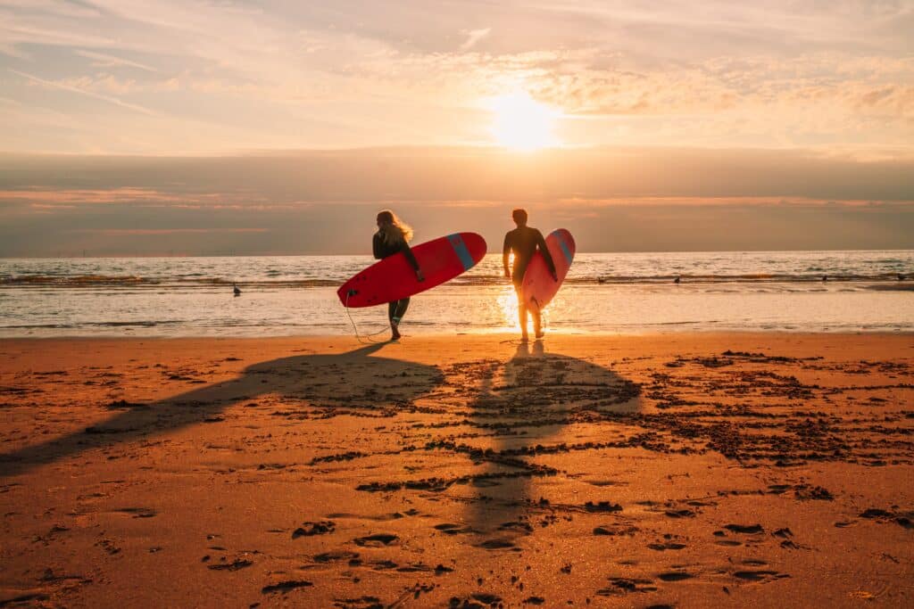 Twee surfers lopen over het strand naar de zee bij zonsondergang. Watersporten in Zandvoort