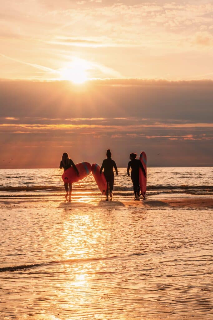 Surfers lopen door de branding met een zonsondergang op de achtergrond