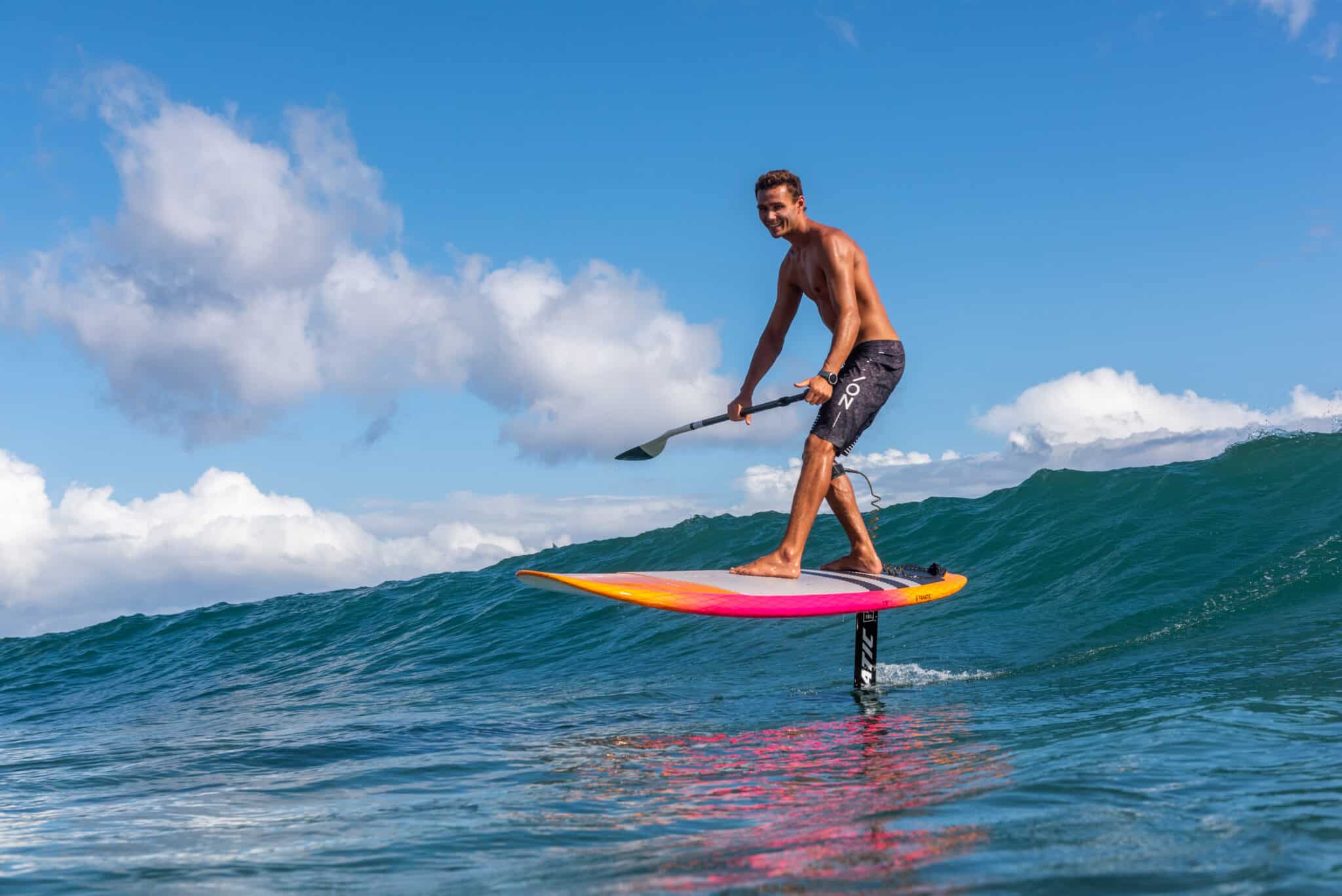 Supfoiler pakt een golf met op een supfoil board met een peddel in zijn handen