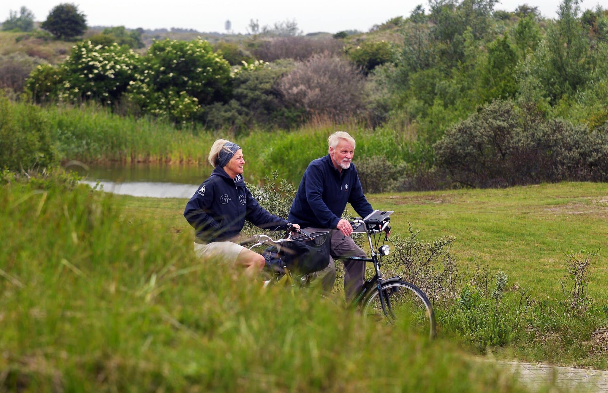 Een ouder stel fietst door de duinen in het voorjaar.