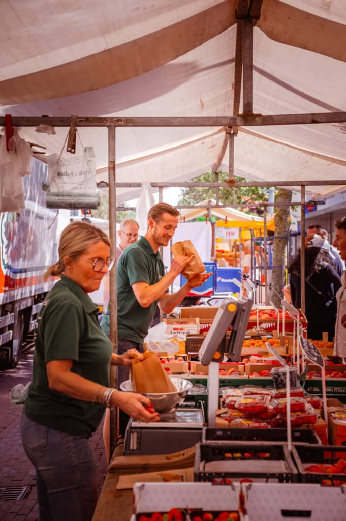Marktverkopers staan bij hun kraam met groente en fruit op de weekmarkt in het centrum van Zandvoort.