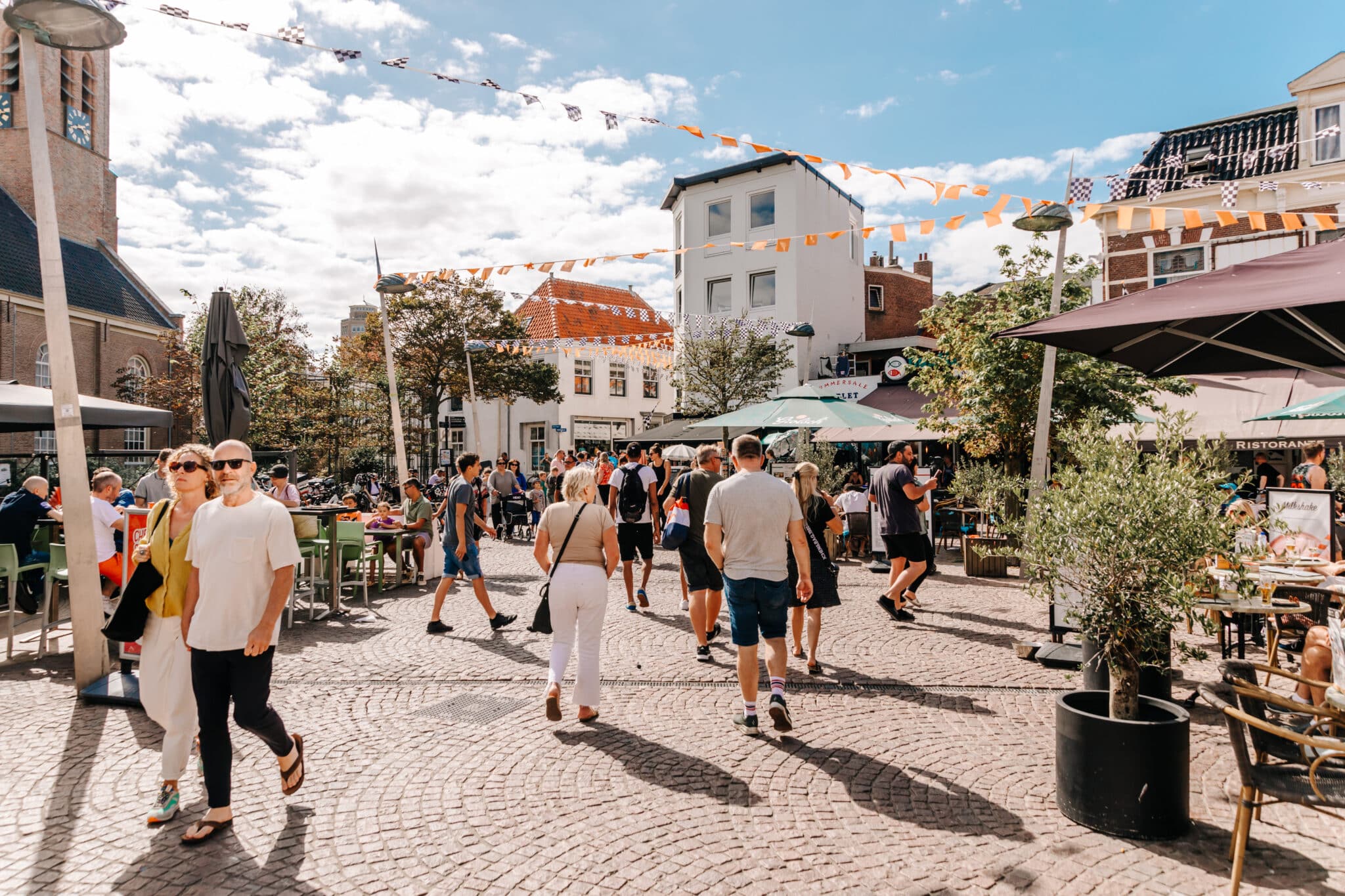 Kerkplein in het dorp Zandvoort, met de kerk op de achtergrond, terrasjes en mensen die op het plein wandelen.