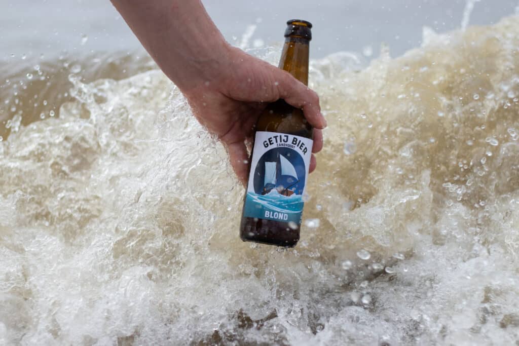 Een Zandvoort blond Getij bier die wordt vastgehouden met de woeste zee op de achtergrond.