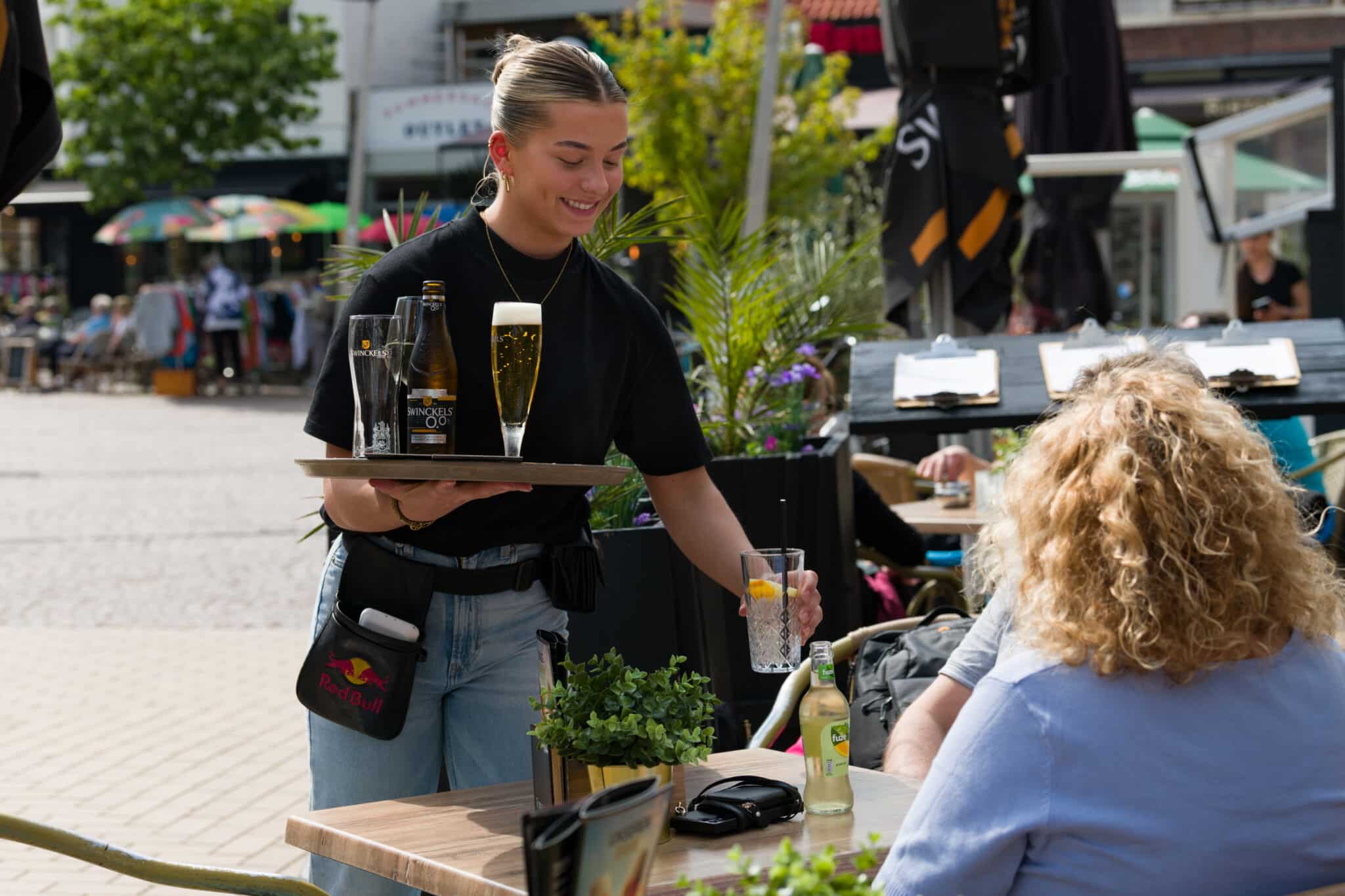 Medewerker serveert drankjes aan gasten op een zonnig terras.