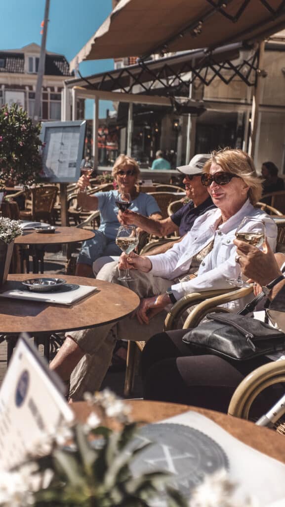 Mensen proosten met een wijntje op een zonnig terras in het centrum van het dorp.
