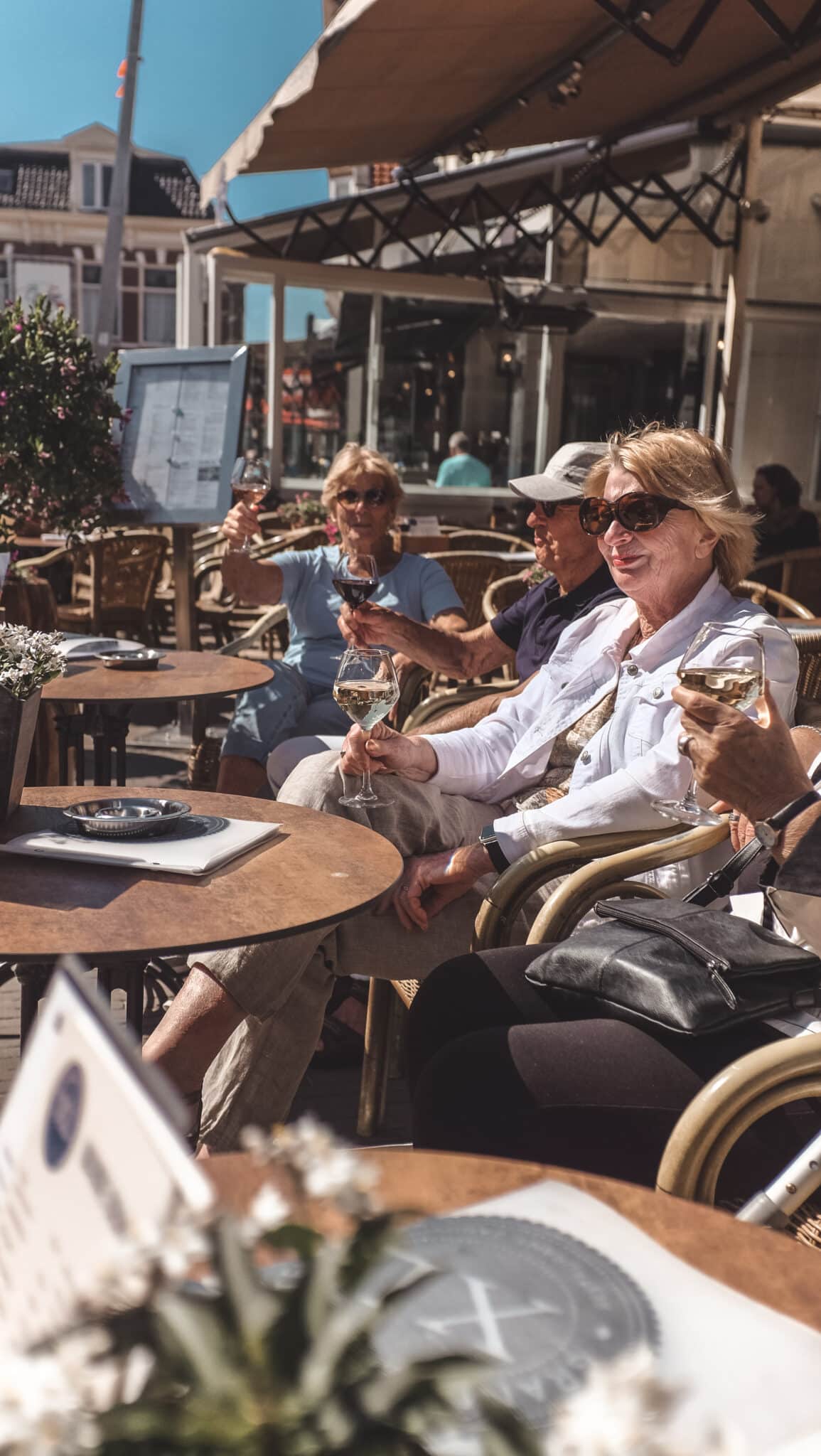 Mensen proosten met een wijntje op een zonnig terras in het centrum van het dorp.