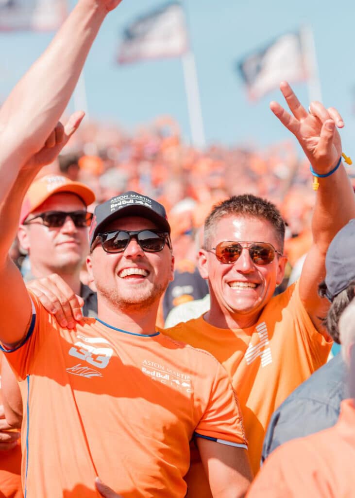 Twee vrienden in oranje gekleed, lachend op de tribune tijdens de Formula 1 Heineken Dutch Grand Prix.