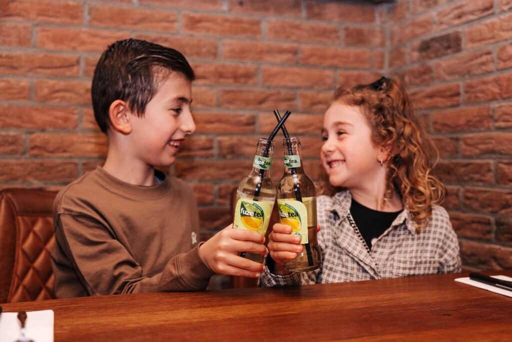 Een jongetje en een meisje die proosten met ice tea in restaurant Andrea