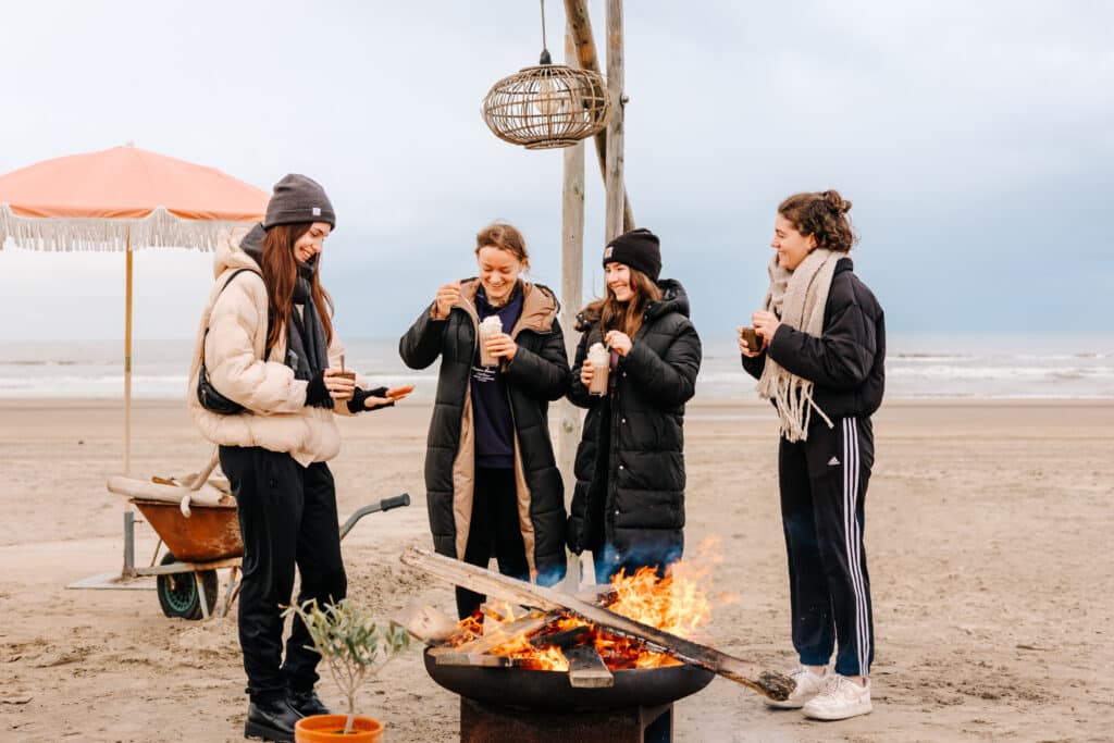 Vier meiden op het strand in de winter bij een vuurtje met warme chocomelk