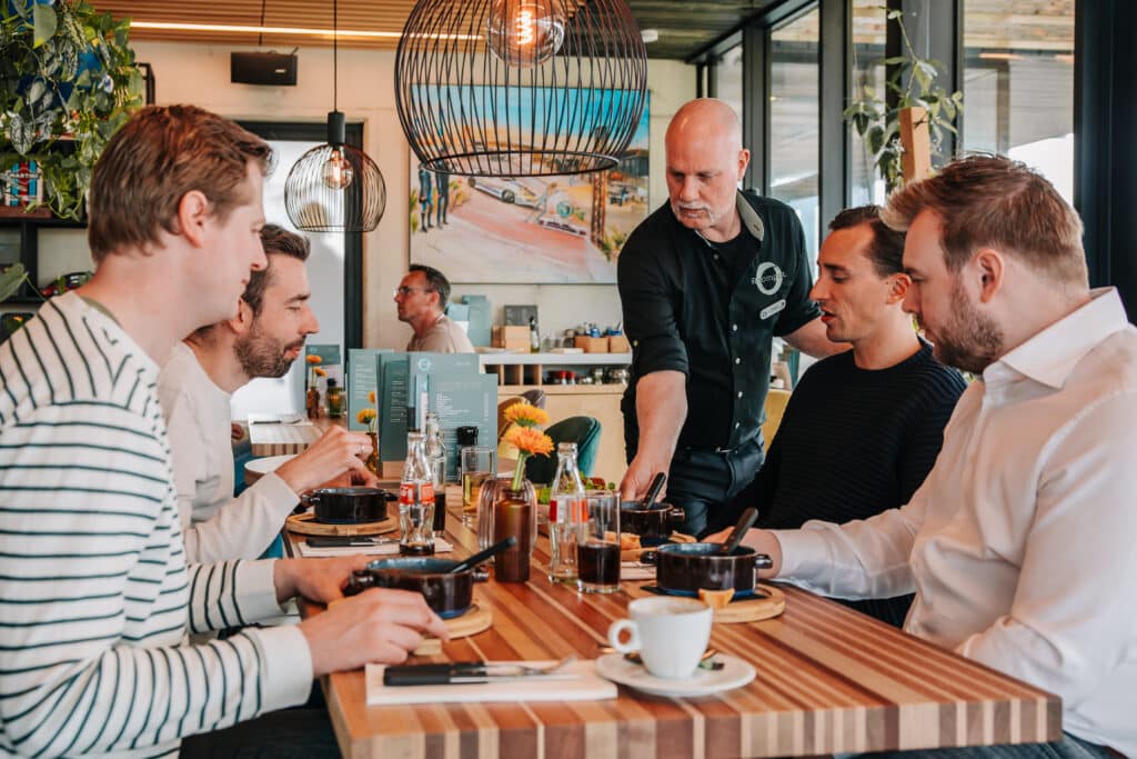 vier mannen krijgen lunch geserveerd in de brasserie van Roompot Zandvoort