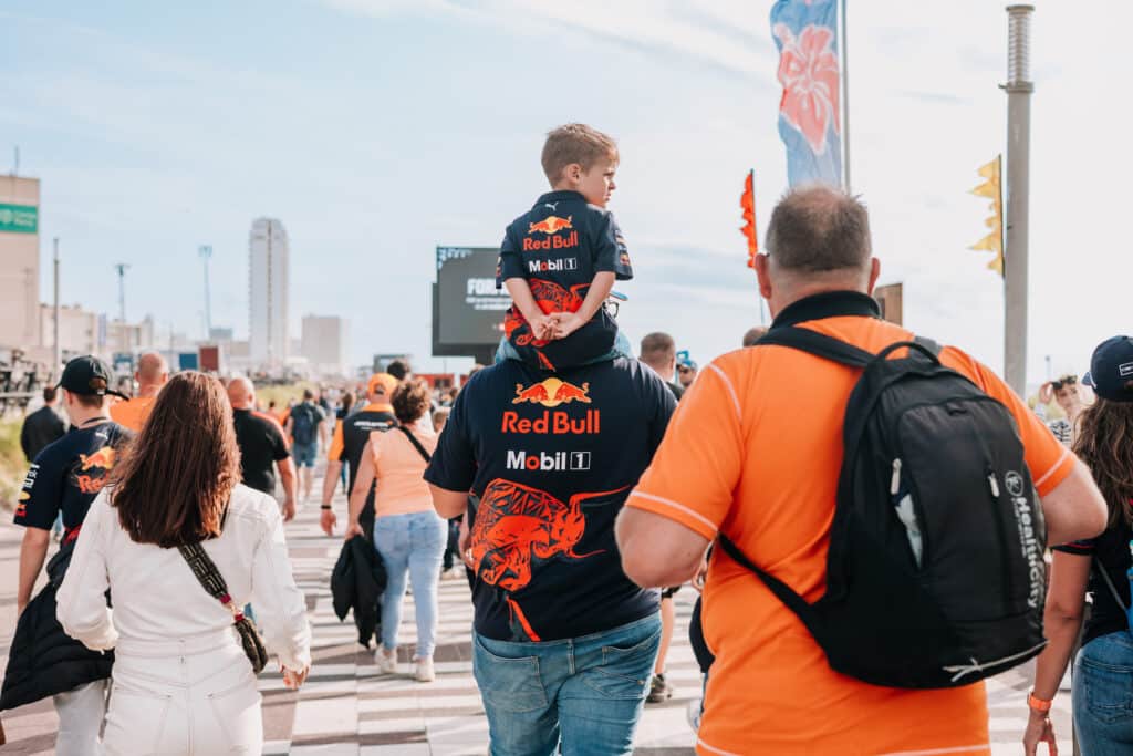 Jongetje in Red Bull-shirt zit op de nek van zijn vader terwijl ze na de Dutch Grand Prix over de boulevard lopen, vanaf Circuit Zandvoort.