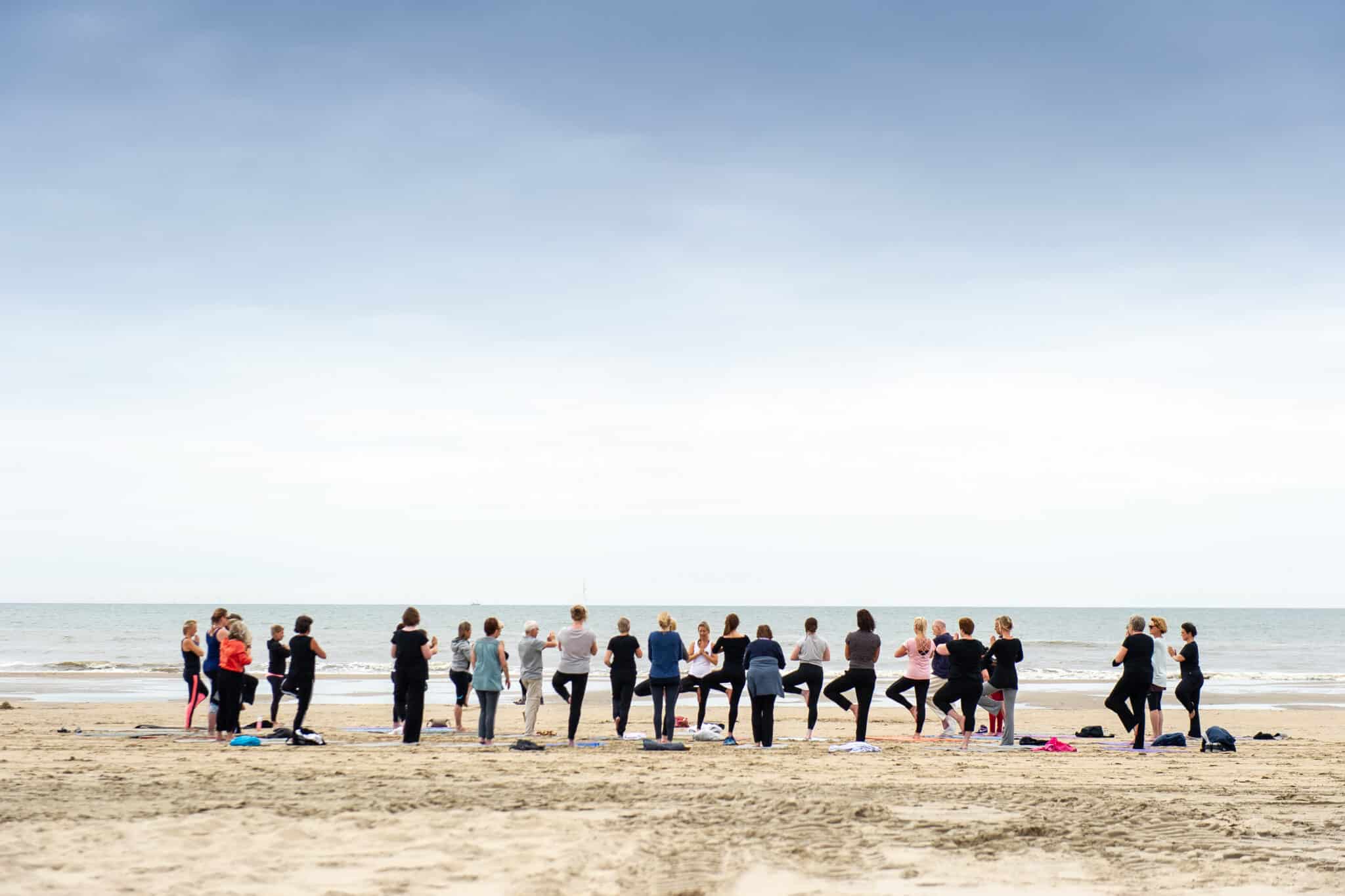 Groep mensen volgt een yoga les op het strand met de zee op de achtergrond