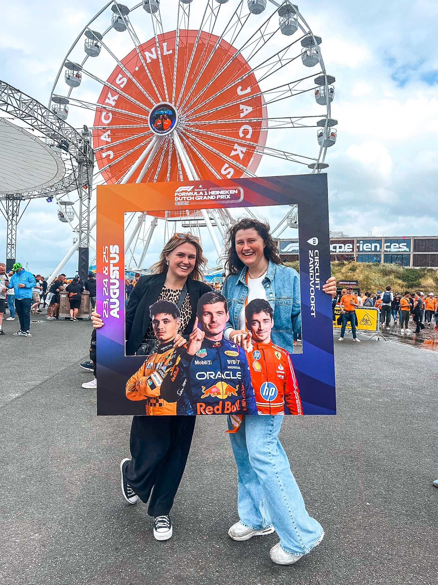 Twee vriendinnen lachen op de foto tijdens de Formula 1 Heineken Dutch Grand Prix, terwijl ze een fotoframe vasthouden op het binnenterrein van het evenement.