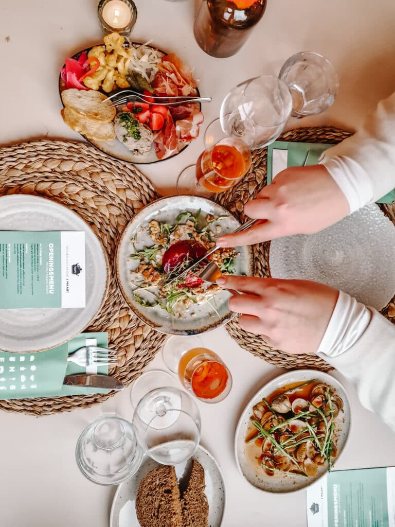 Gedekte tafel waarbij 2 vrouwen handen eten aansnijden