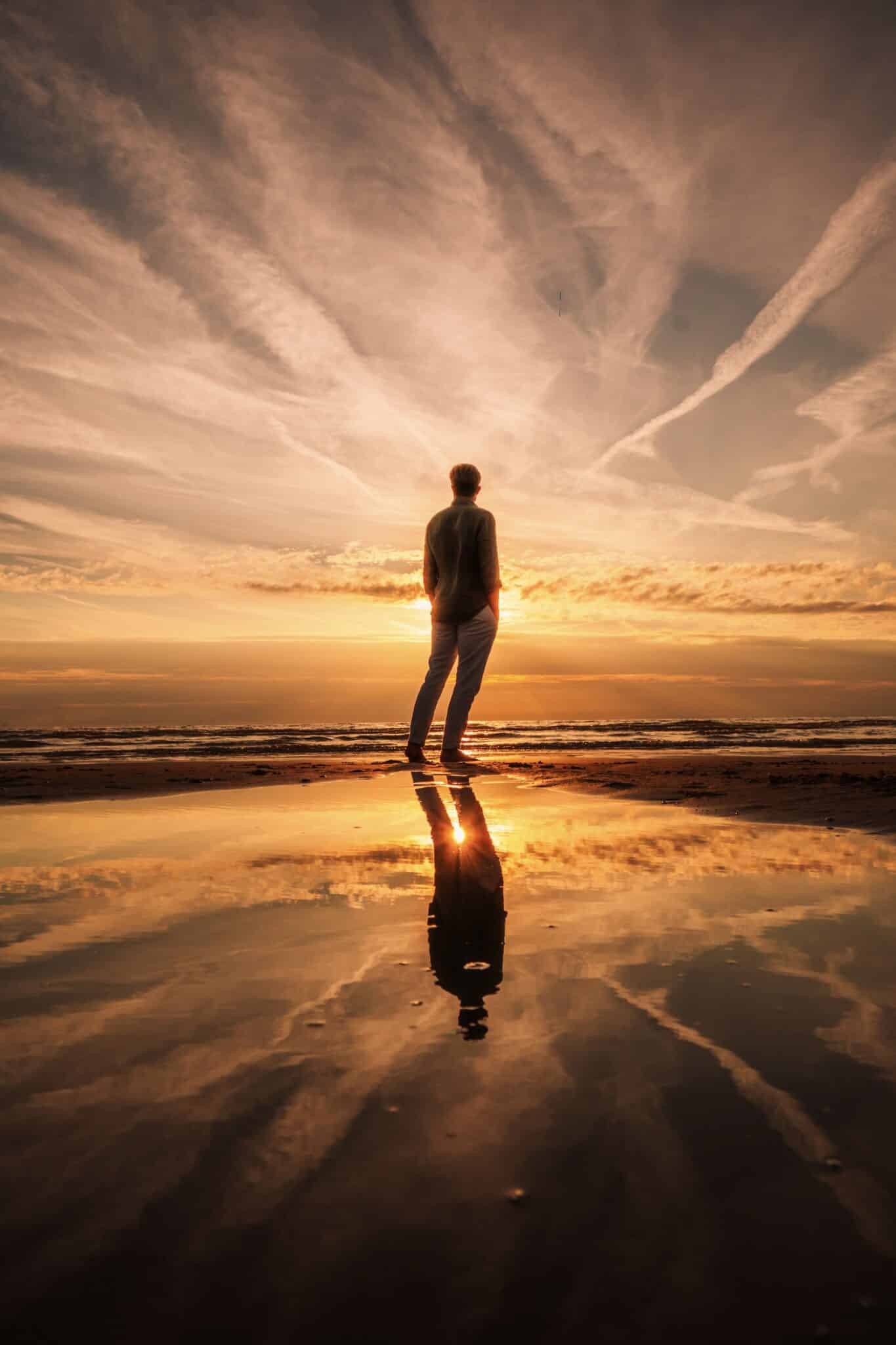 Man op het strand kijkt bij zonsondergang naar de ondergaande zon