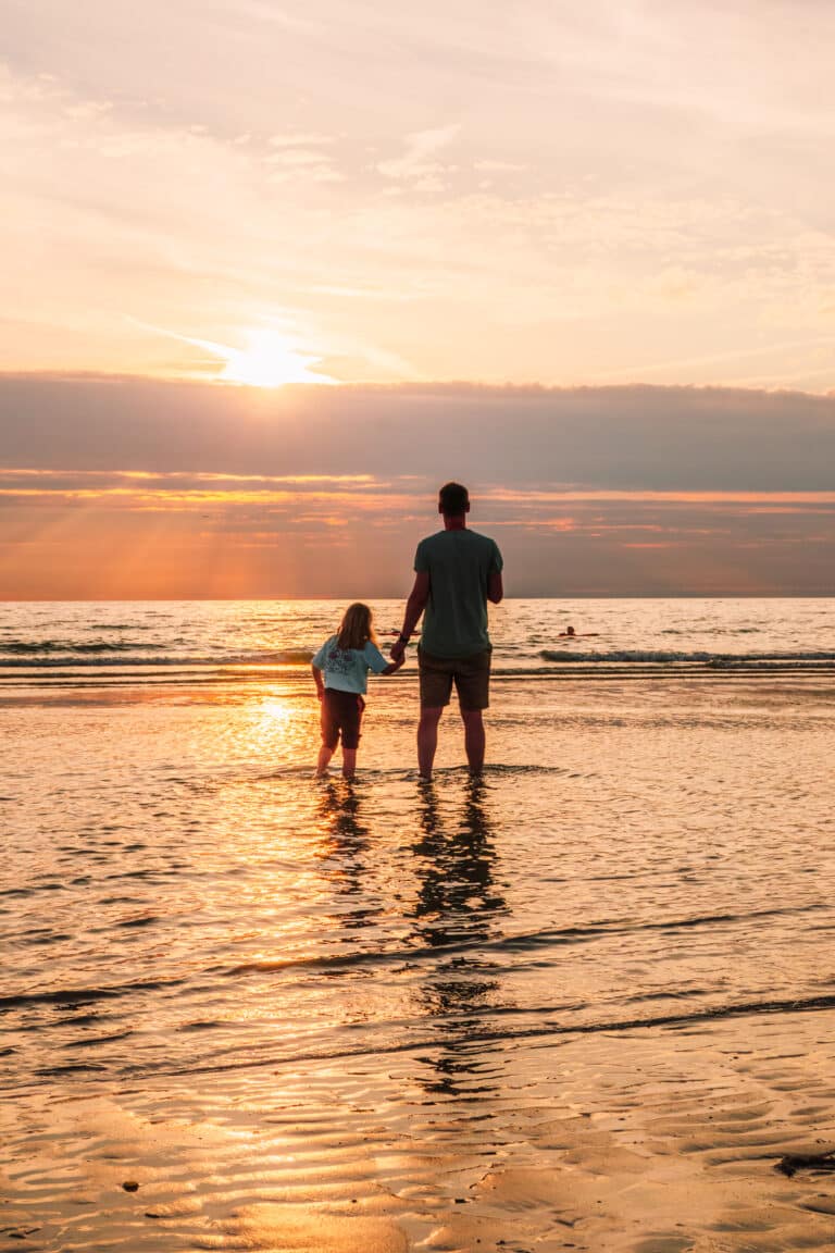 Vader met kind tijdens een weekend in Zandvoort in de branding kijkend naar de ondergaande zon op het strand van Zandvoort