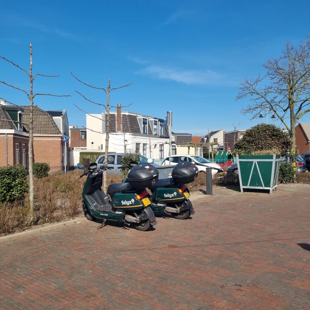 Twee deelscooters van het merk Felyx naast elkaar geparkeerd op de stoep in het centrum van Zandvoort