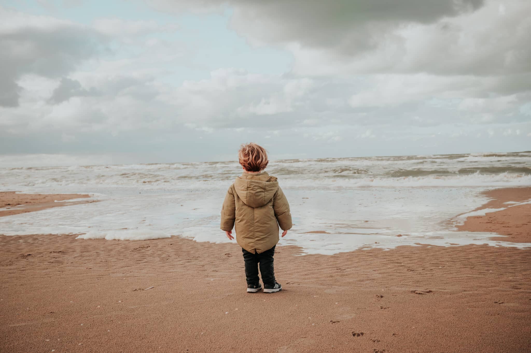 Klein jongetje die kijkt naar de zee in de winter in zandvoort