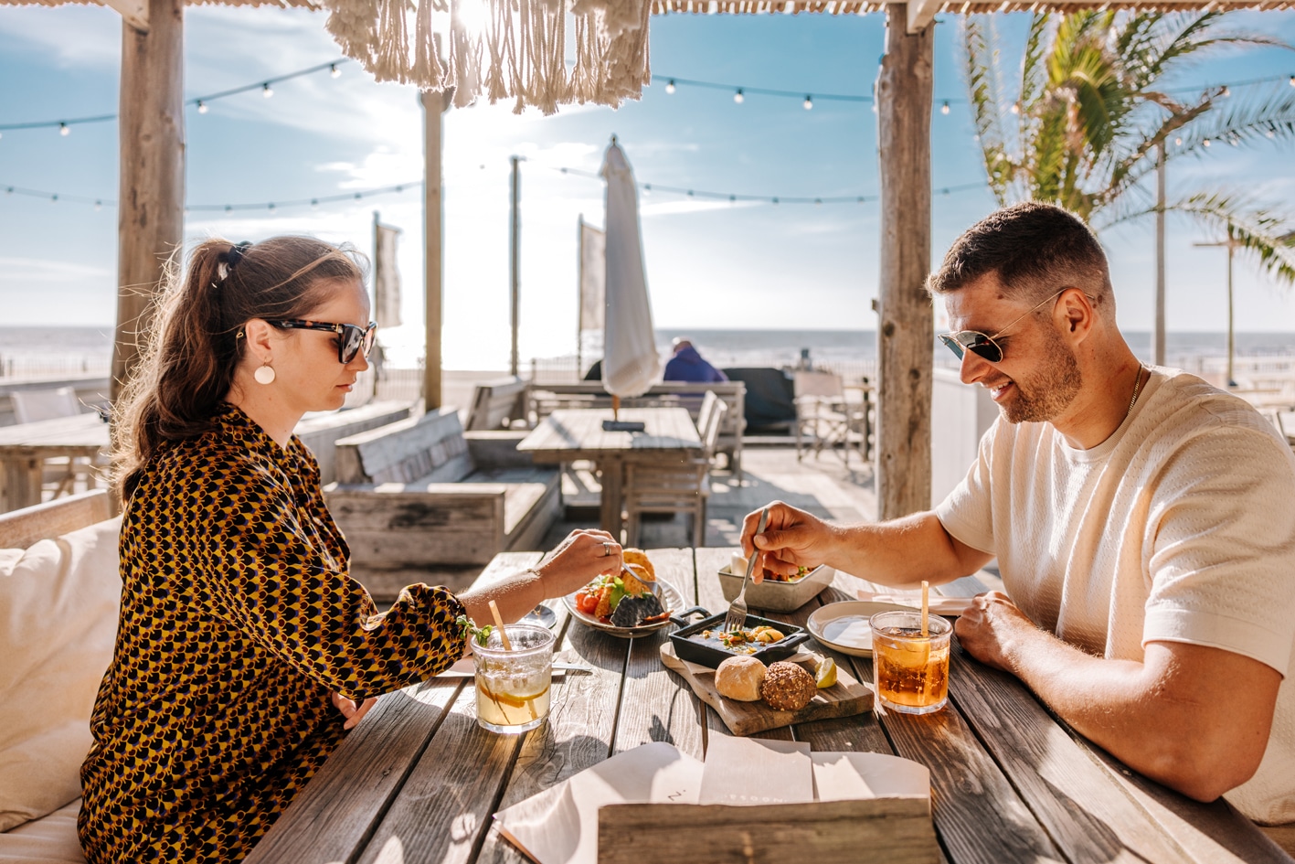 Een vrouw en man dineren in de zomer bij Strandpaviljoen Noosa met een laagstaande, ondergaande zon op de achtergrond boven de zee