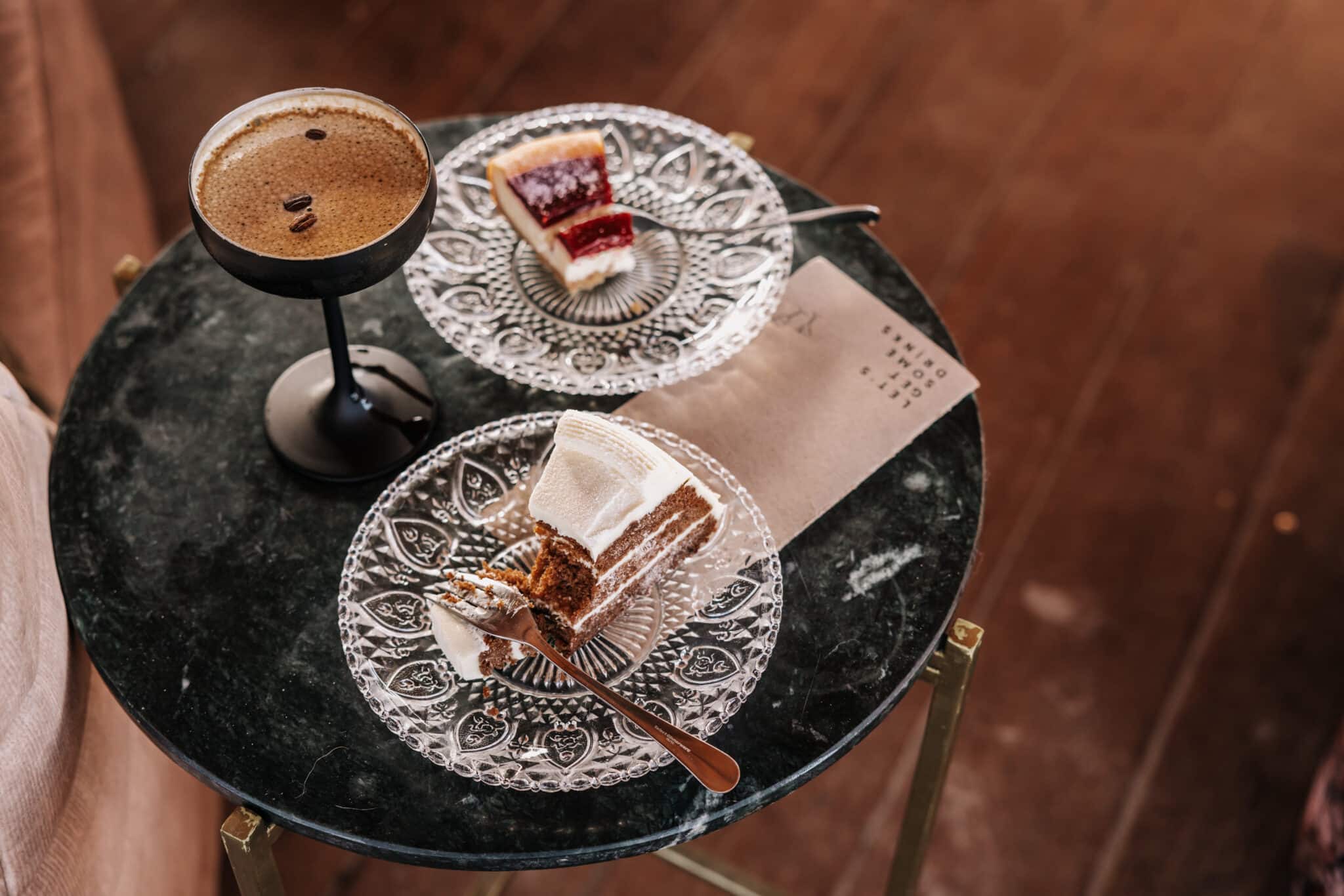 Espresso Martini op een marmeren tafeltje met twee stukjes taart op mooie glazen bordjes