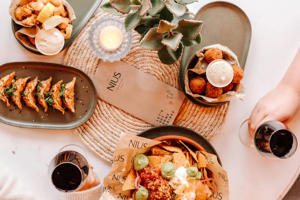lichte tafel met verschillende kleine gerechten en rode wijn, daarnaast ligt de menukaart van Nius Beach House