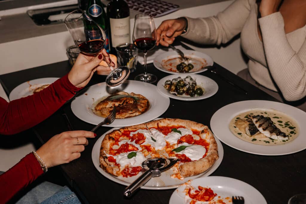 Tafel vol met eten, van pizza tot heerlijke vis en olijven, er wordt geproost met rode wijn