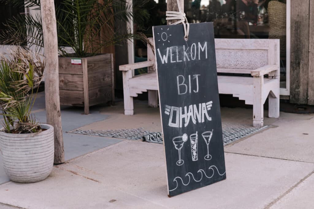 Krijtbord bij strandtent Ohana, met daarop Welkom bij Ohana en een tekening van drie cocktailglazen
