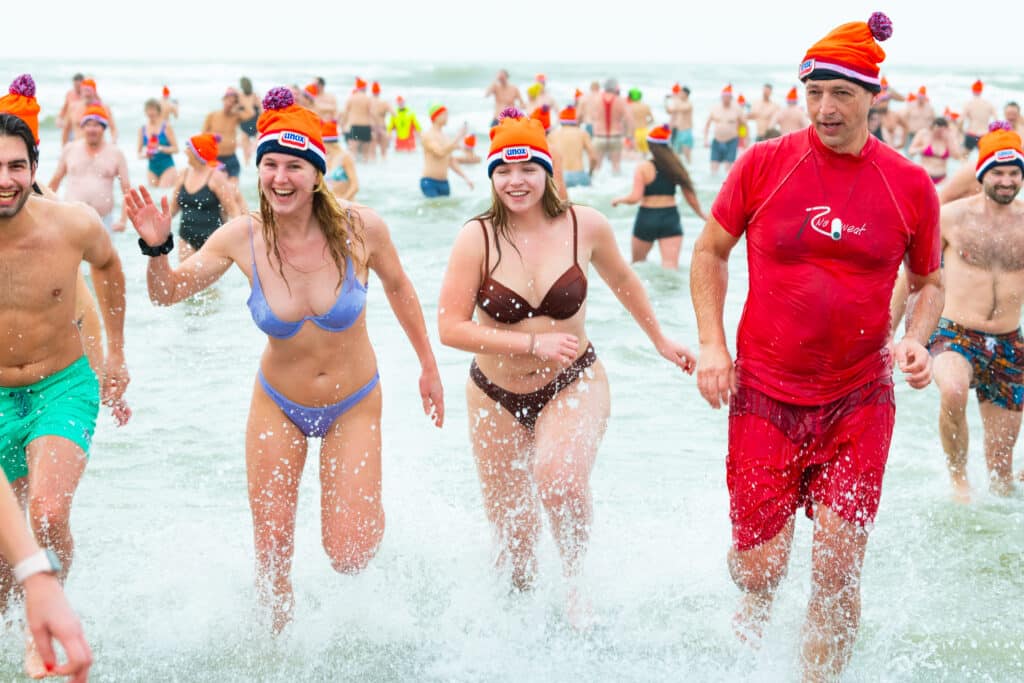 Lachende mensen komen de zee uit met een Unox-muts tijdens het evenement de Nieuwjaarduik in Zandvoort. Zandvoort