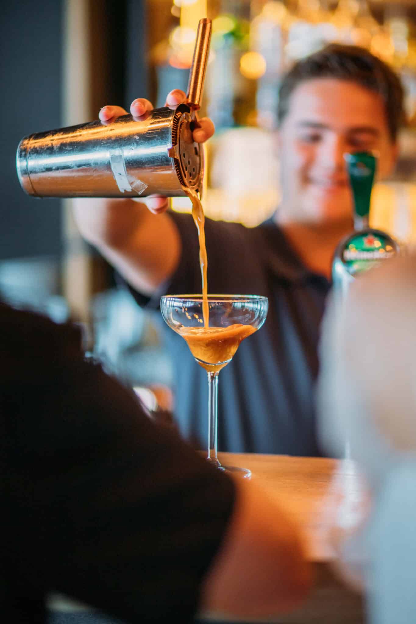 Barman die een espresso martini vanuit de cocktailshaker in het cocktailglas schenkt
