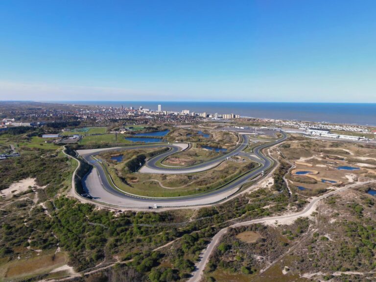Spectaculair dronebeeld van het circuit Zandvoort, omringd door duinen en met de zee op de achtergrond.