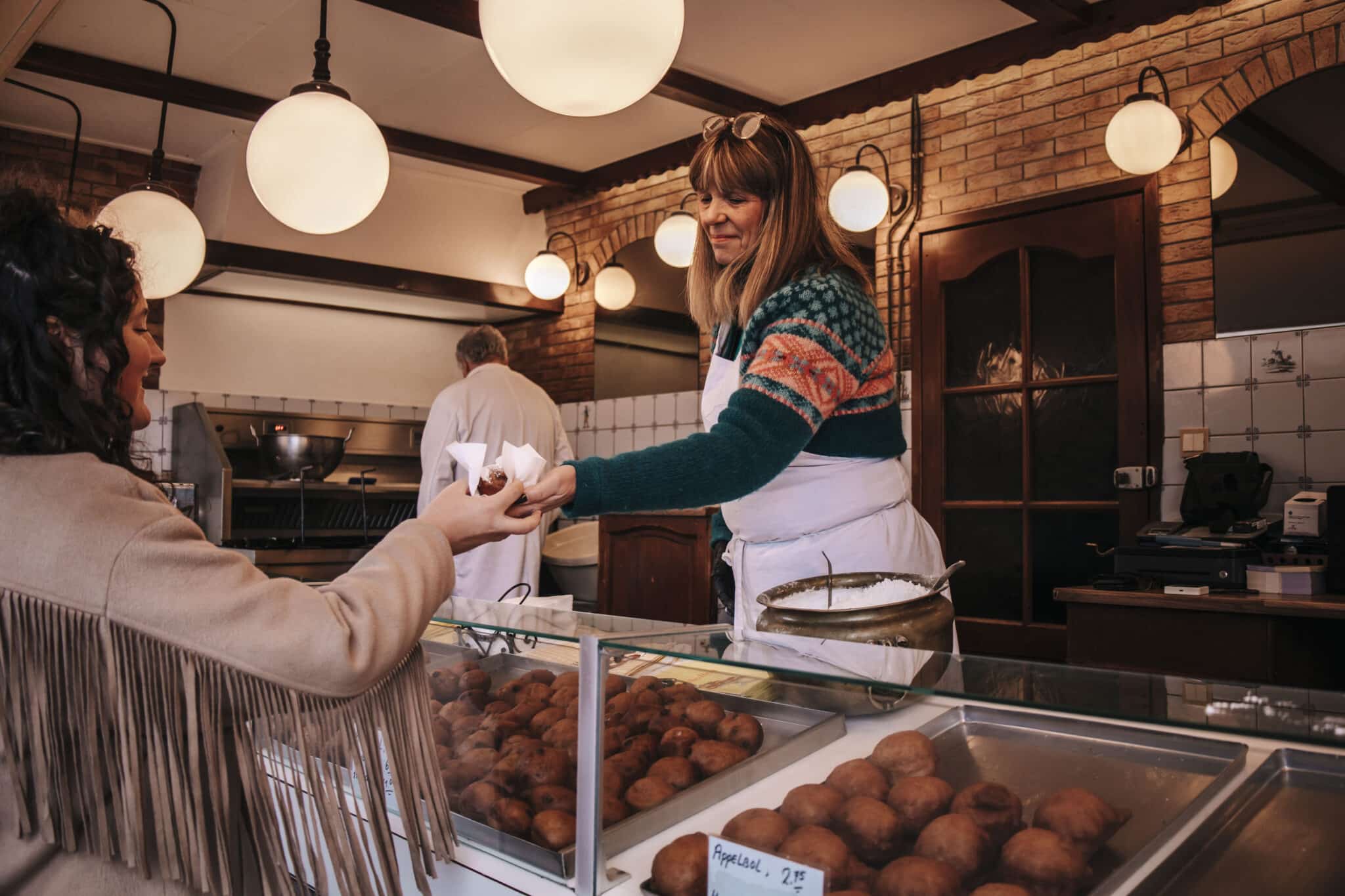 Oliebollenkraam in het centrum van Zandvoort in de winter. De medewerkster rijkt een oliebol uit naar de koper.