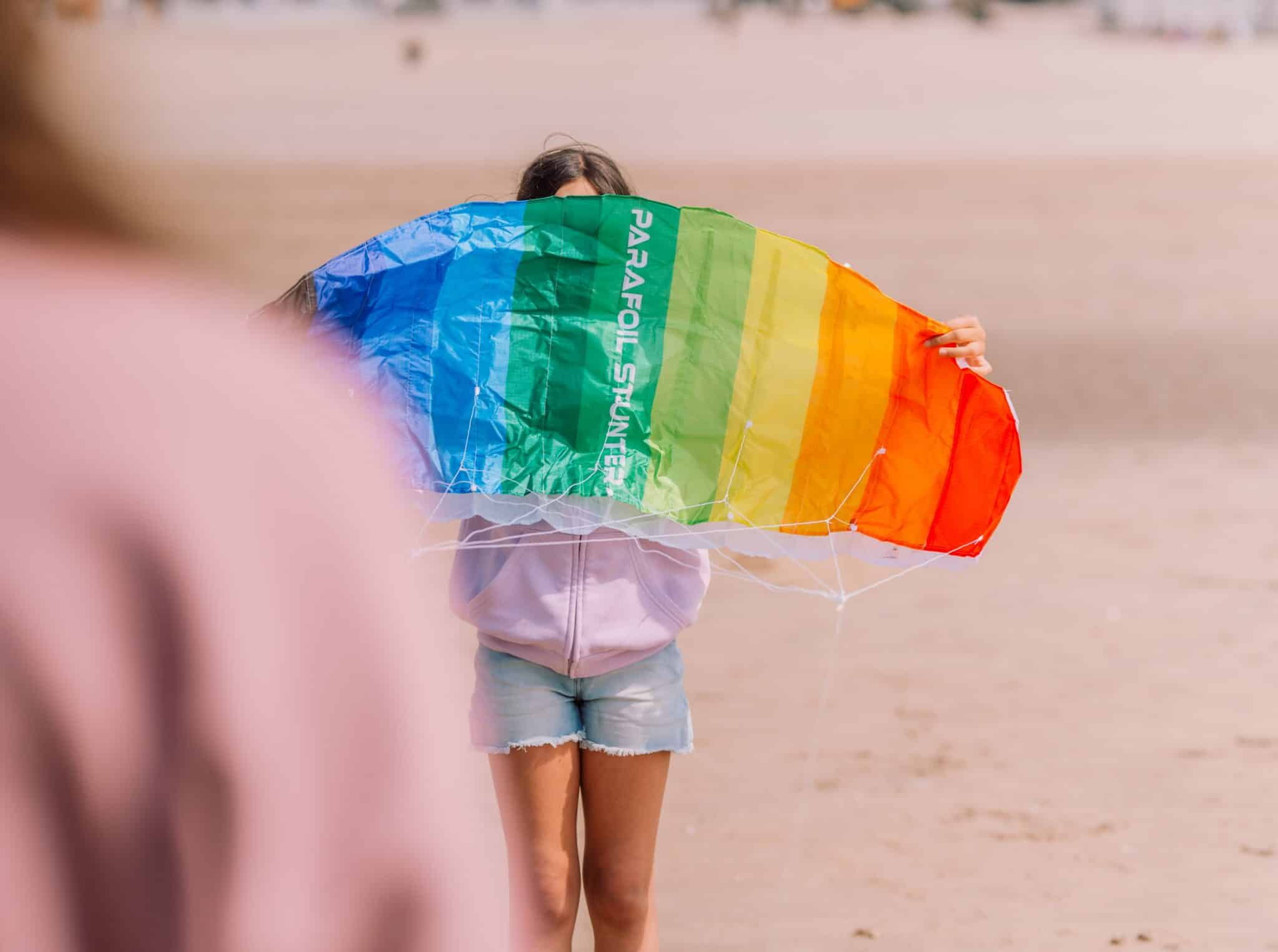 Meisje met een regenboog vlieger op het strand