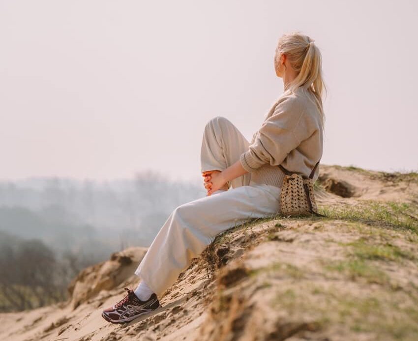 Vrouw zit op de rand van een duin en geniet van de zon