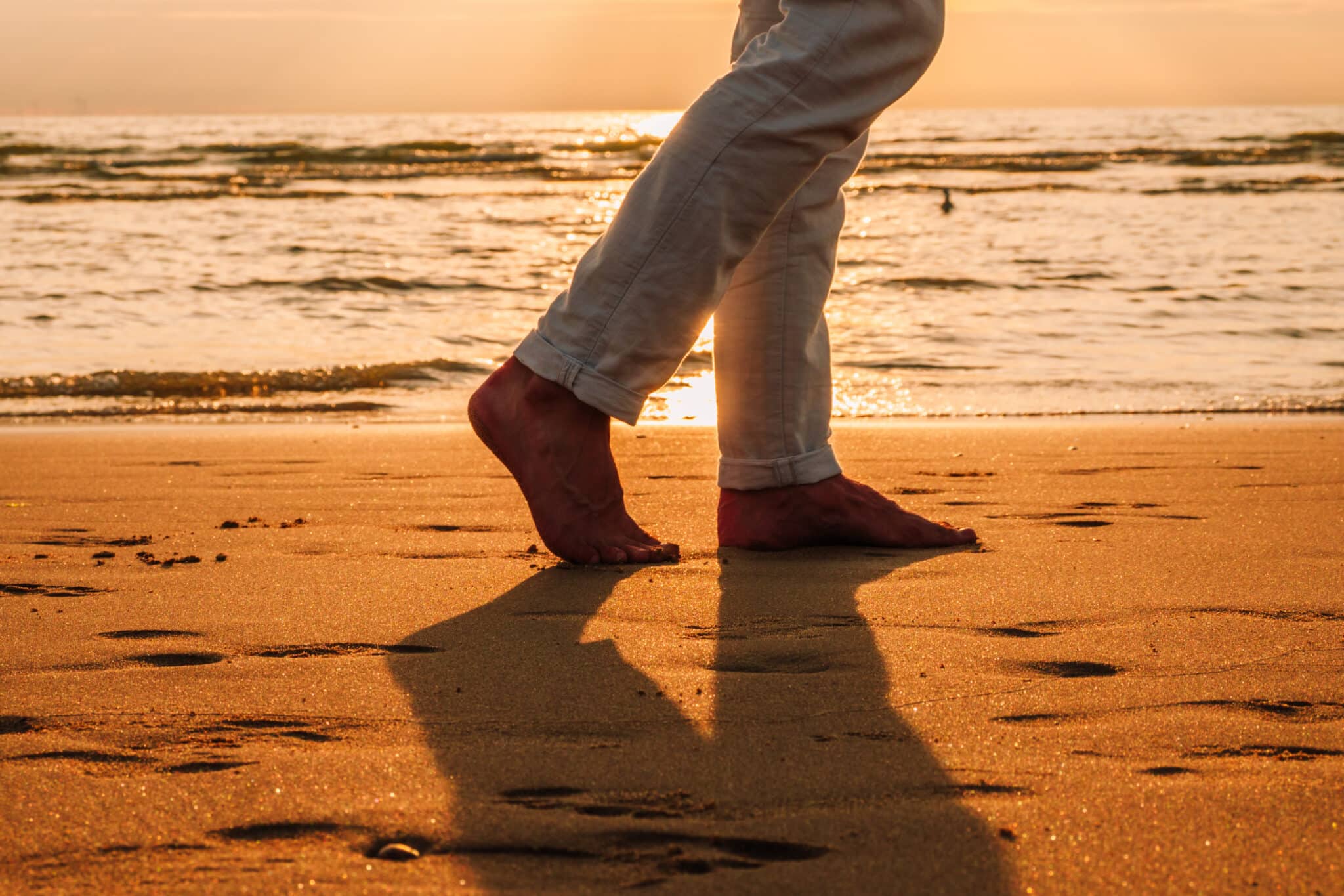 Voeten van een man die wandelt over het Zandvoortse strand bij zonsondergang