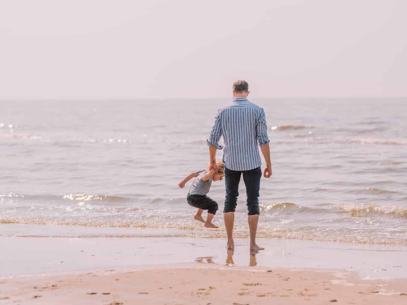Jongetje met zijn vader op het strand. Waarbij het jongetje in de zee springt